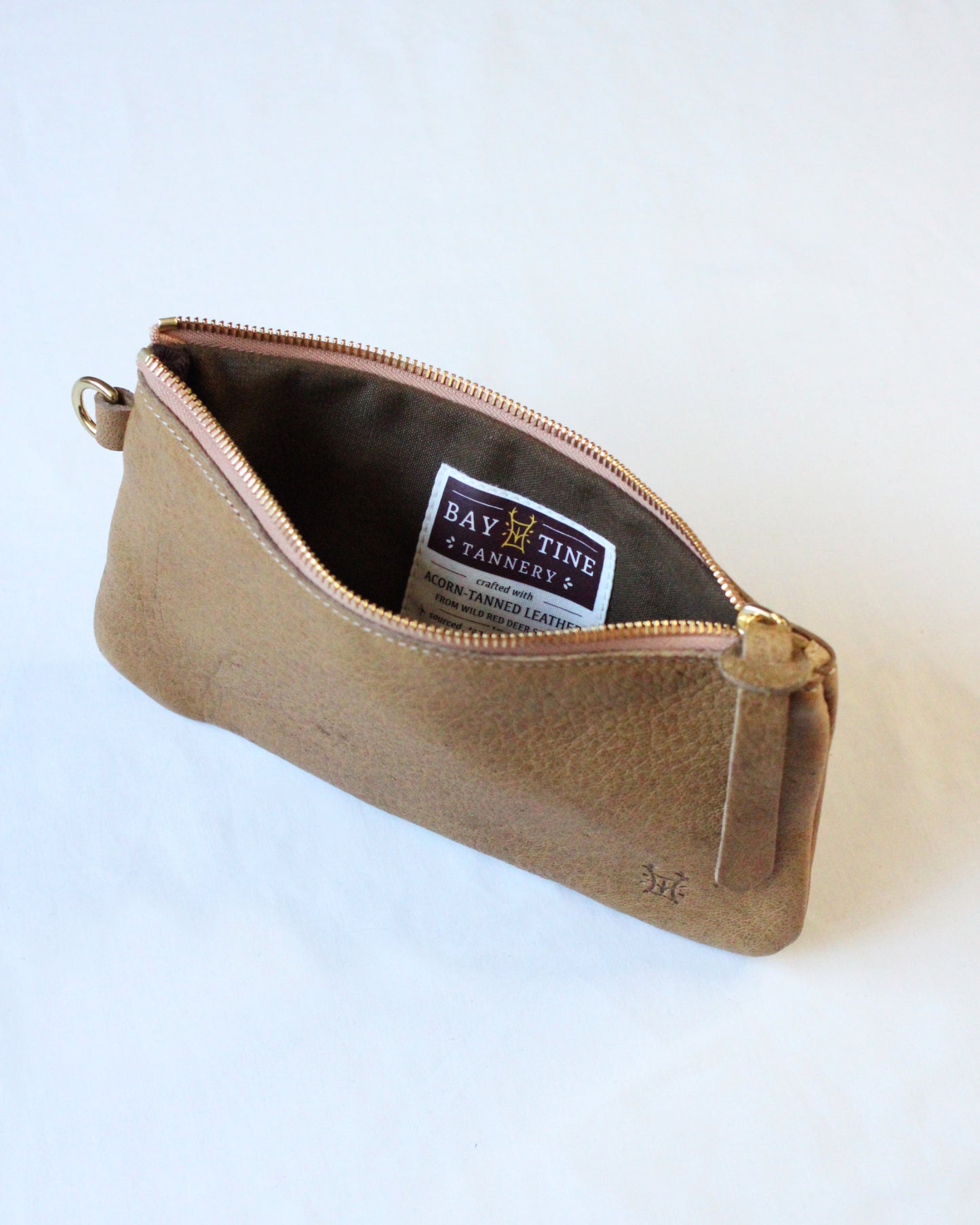 Brown zip pouch with "Acorn" embossed logo by BAY TINE TANNERY, made of leather, featuring a metal zipper and compact design.